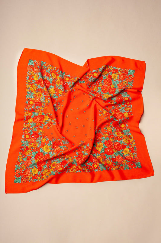 Red square scarf with a floral border featuring yellow and orange flowers and green leaves on a light background.
