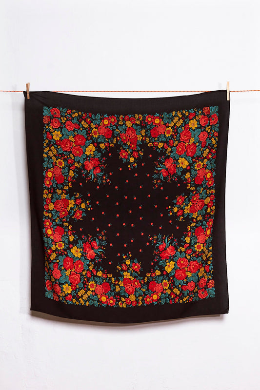 Pañuelo cuadrado negro con estampado tradicional de flores rojas, amarillas y verdes, colgado de una cuerda.