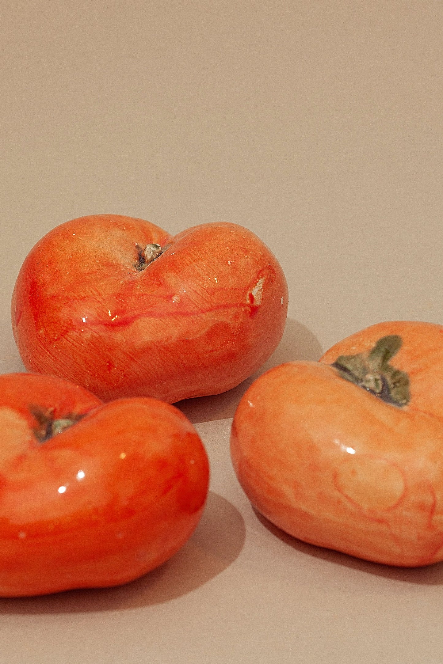 Tres cerámicas brillantes en color naranja, con forma de tomate, sobre fondo beige. Ideal para decoración moderna.