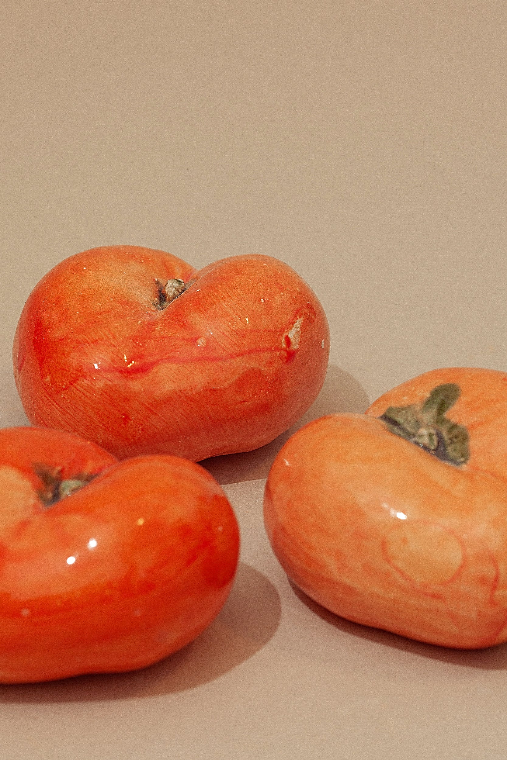 Tres cerámicas brillantes en color naranja, con forma de tomate, sobre fondo beige. Ideal para decoración moderna.