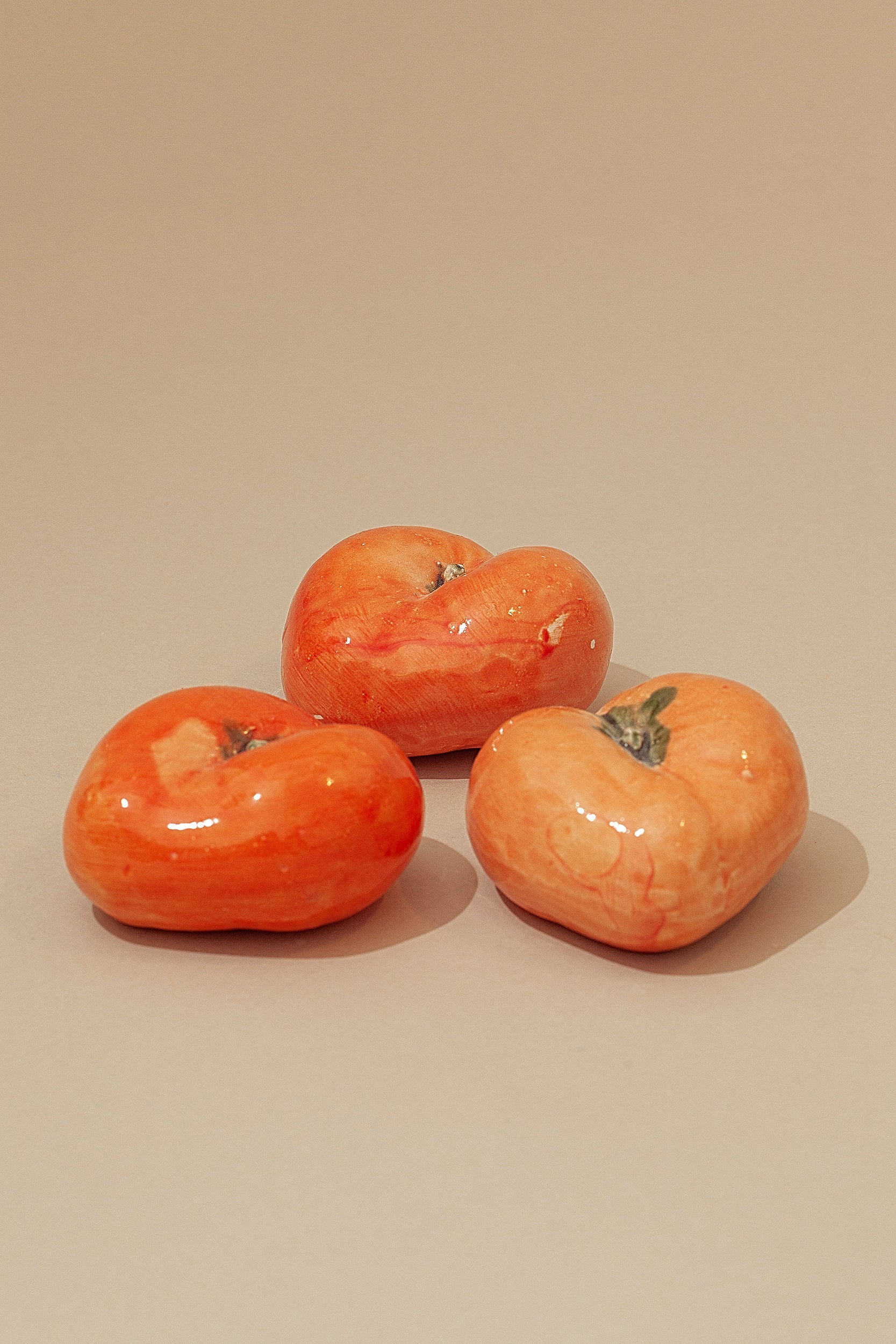 Tres tomates cerámicos de color naranja brillante, con un acabado esmaltado y detalles realistas.