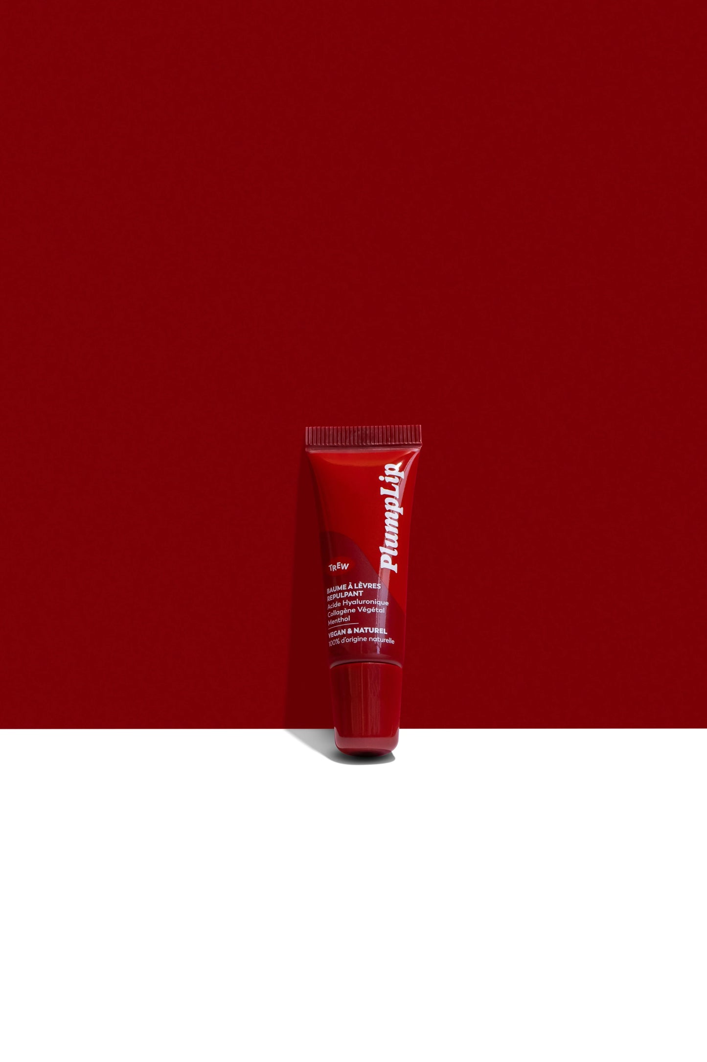 Tube rouge vif de baume PlumpLip Trew Cosmetic sur fond bicolore rouge et blanc, typographie blanche verticale.