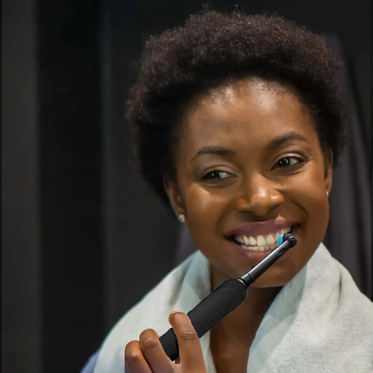 A person smiling while using a matte black electric rotary toothbrush with a blue-tipped round brush head.
