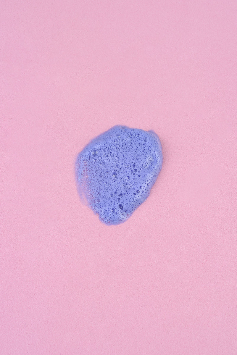 Espuma de baño color lila sobre fondo rosa, textura suave y cremosa, ideal para un momento de relajación.