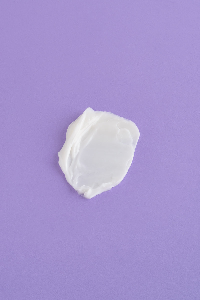 Crema hidratante blanca sobre fondo morado, textura suave y cremosa, ideal para todo tipo de piel.