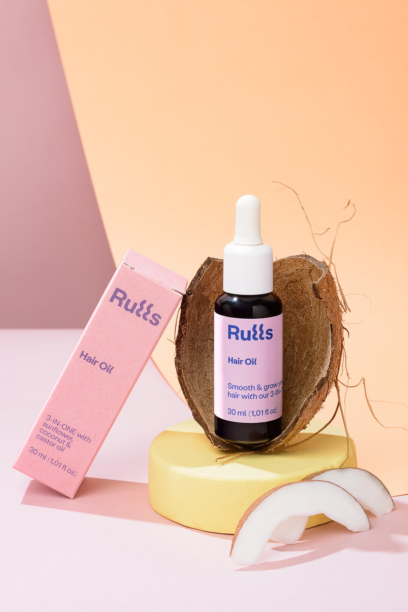 Aceite para el cabello Ruüts, 30 ml, en frasco negro con gotero, sobre fondo rosa y amarillo, envase en caja rosa.