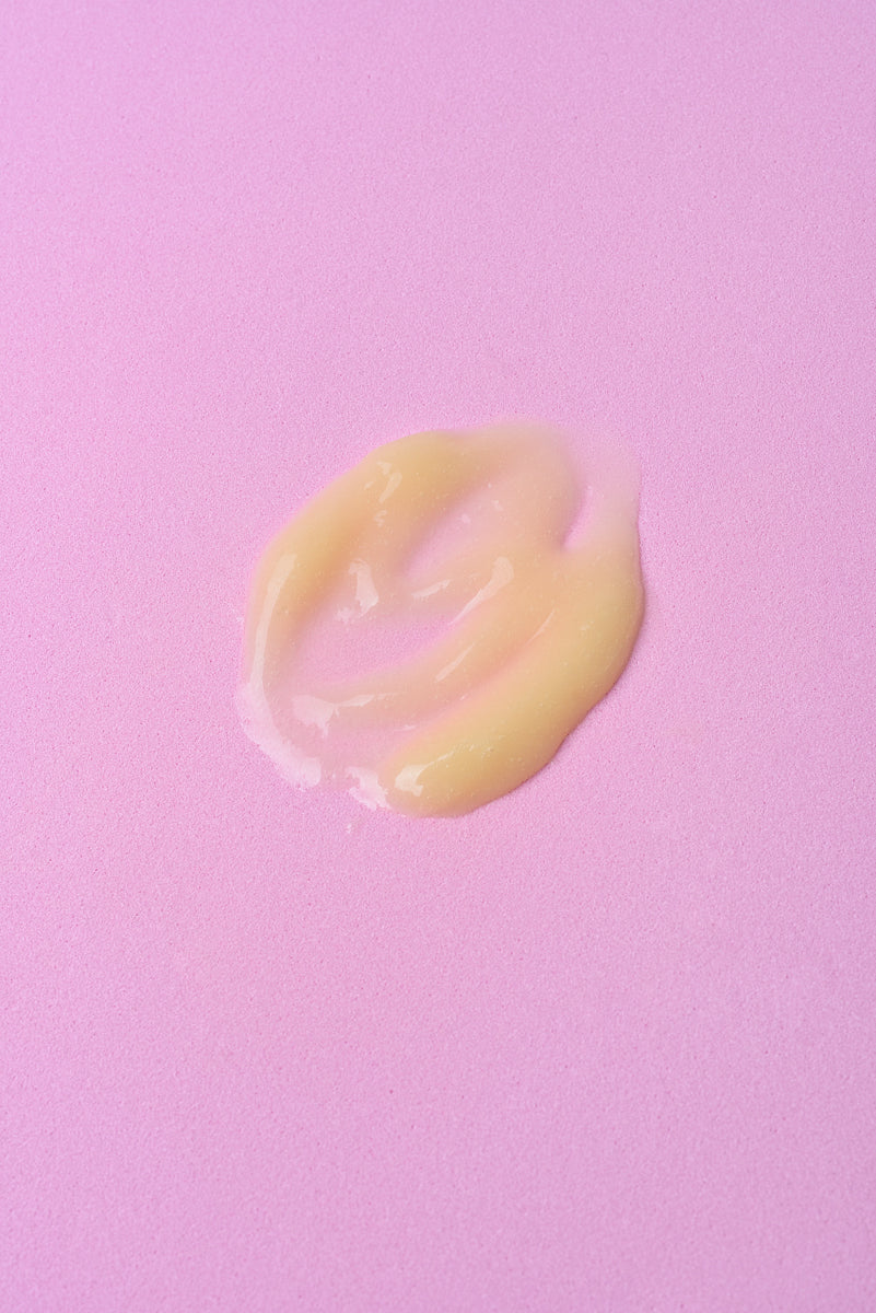 Crema hidratante amarilla en textura suave sobre fondo rosa. Ideal para piel seca y sensible.