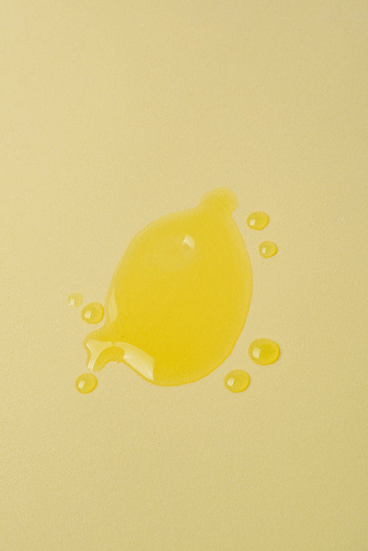 Gota de aceite amarillo brillante sobre fondo amarillo suave, ideal para productos de belleza o cocina.