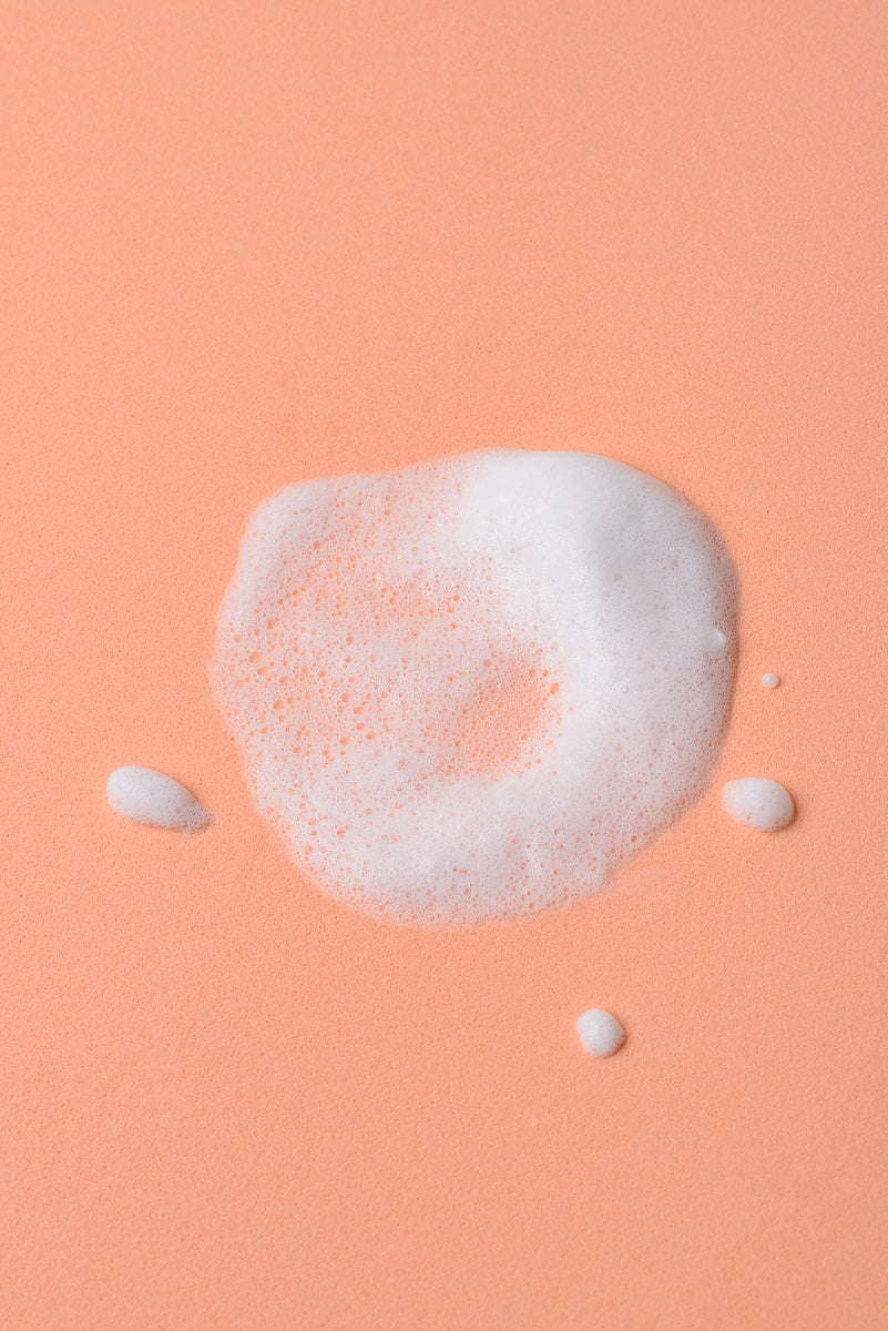 Espuma blanca sobre fondo melocotón, ideal para productos de limpieza o cuidado personal.