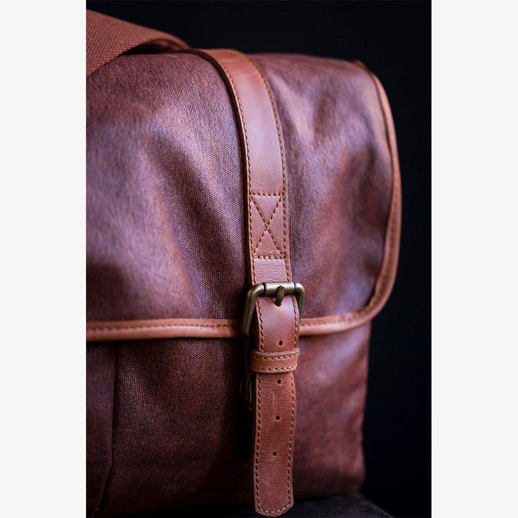 Close-up of a handmade waxed canvas camera bag with a leather strap and buckle details.