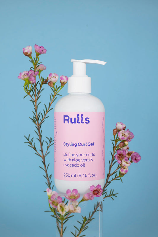 Gel de rizos Ruúls, envase blanco y rosa, 250 ml, con aloe vera y aceite de aguacate en fondo azul.