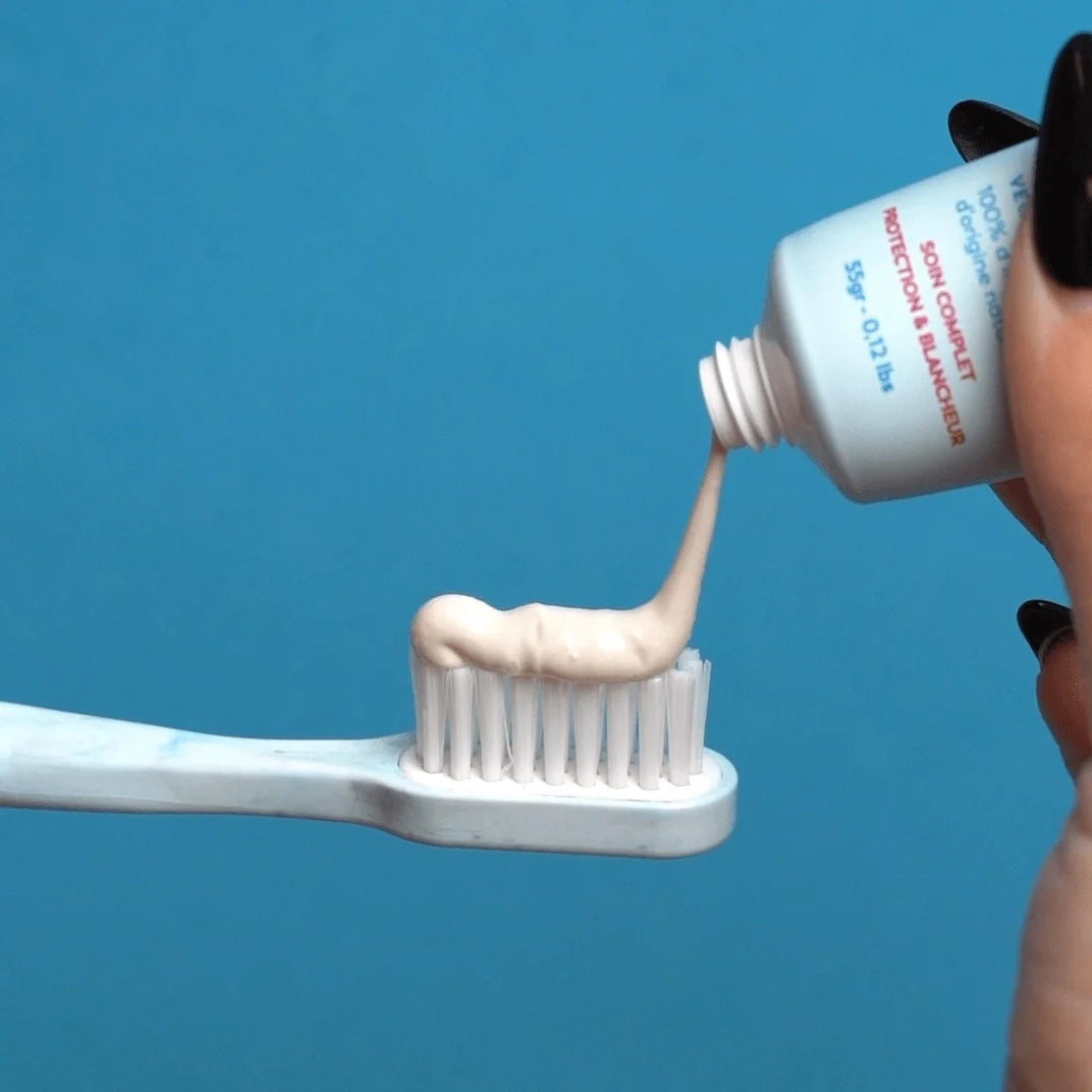 Dentifrice beige crémeux Trew Cosmetic pressé sur une brosse à dents, sur fond bleu vif.