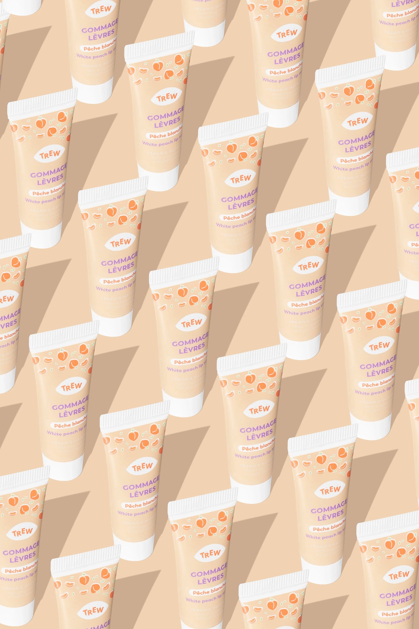 Multiples tubes de gommage lèvres Trew Cosmetic beiges, imprimés de pêches, disposés en diagonale sur fond pêche.
