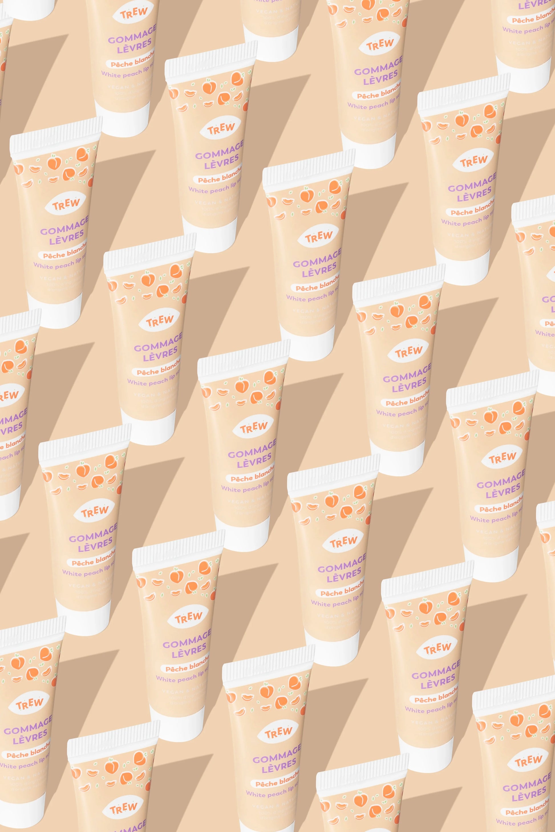 Multiples tubes de gommage lèvres Trew Cosmetic beiges, imprimés de pêches, disposés en diagonale sur fond pêche.
