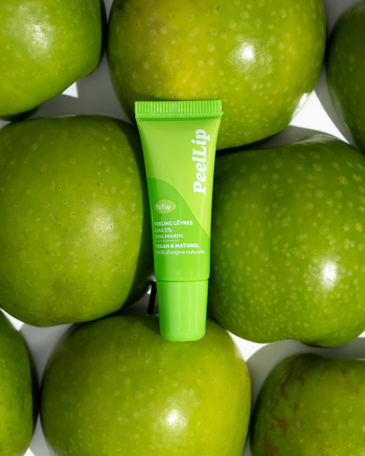 Lime green squeeze tube of PeelLip lip exfoliant centered amongst several fresh, bright green apples.