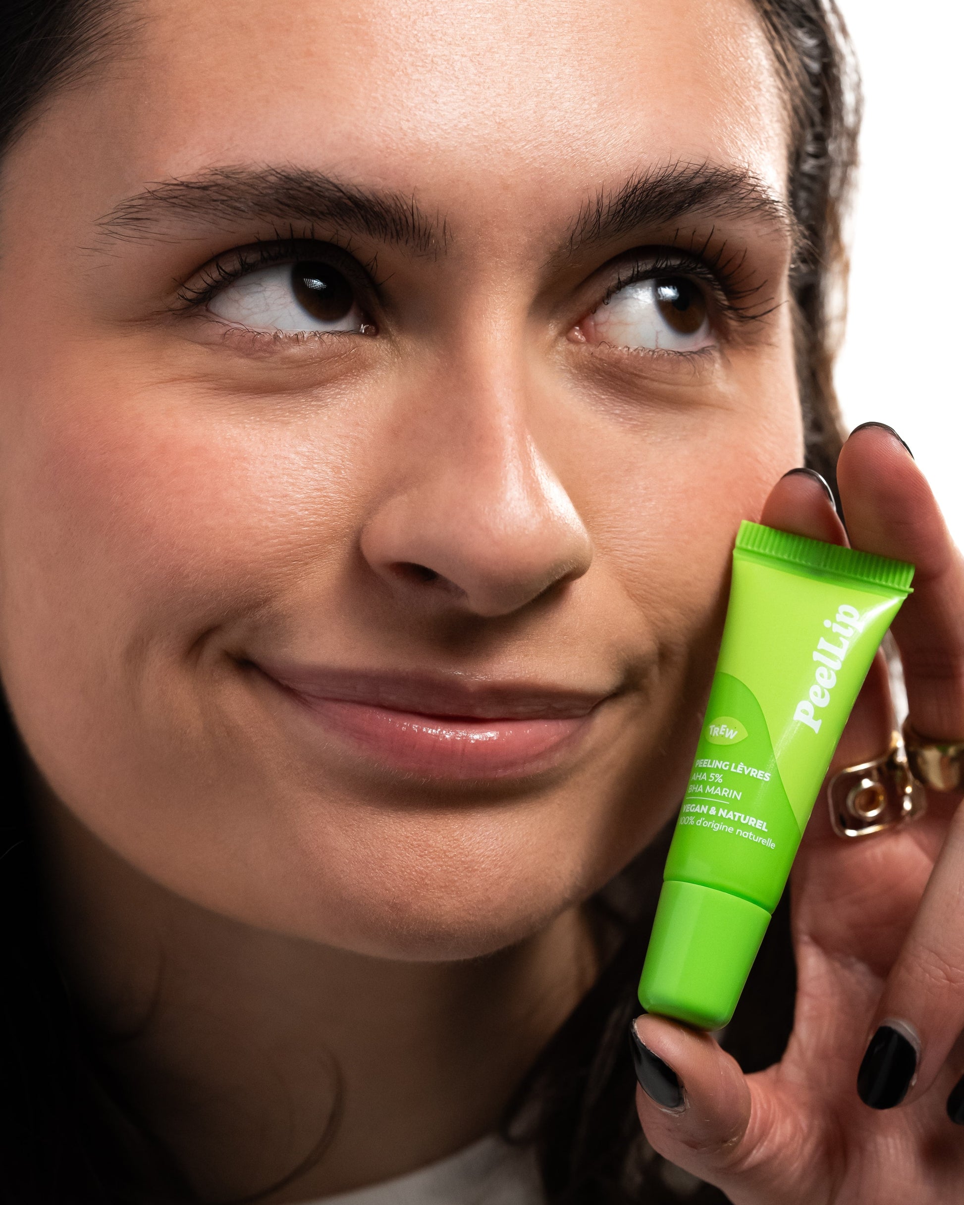 A woman holds a bright green tube of PeelLip 5% AHA & BHA Marin lip exfoliant near her face.