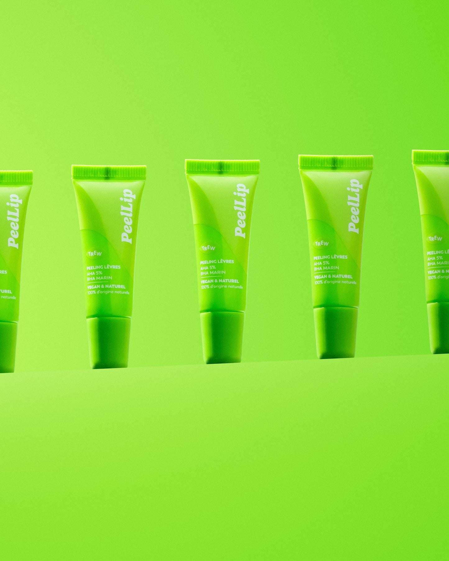 Several bright green lip exfoliant squeeze tubes standing in a row against a matching lime green background.