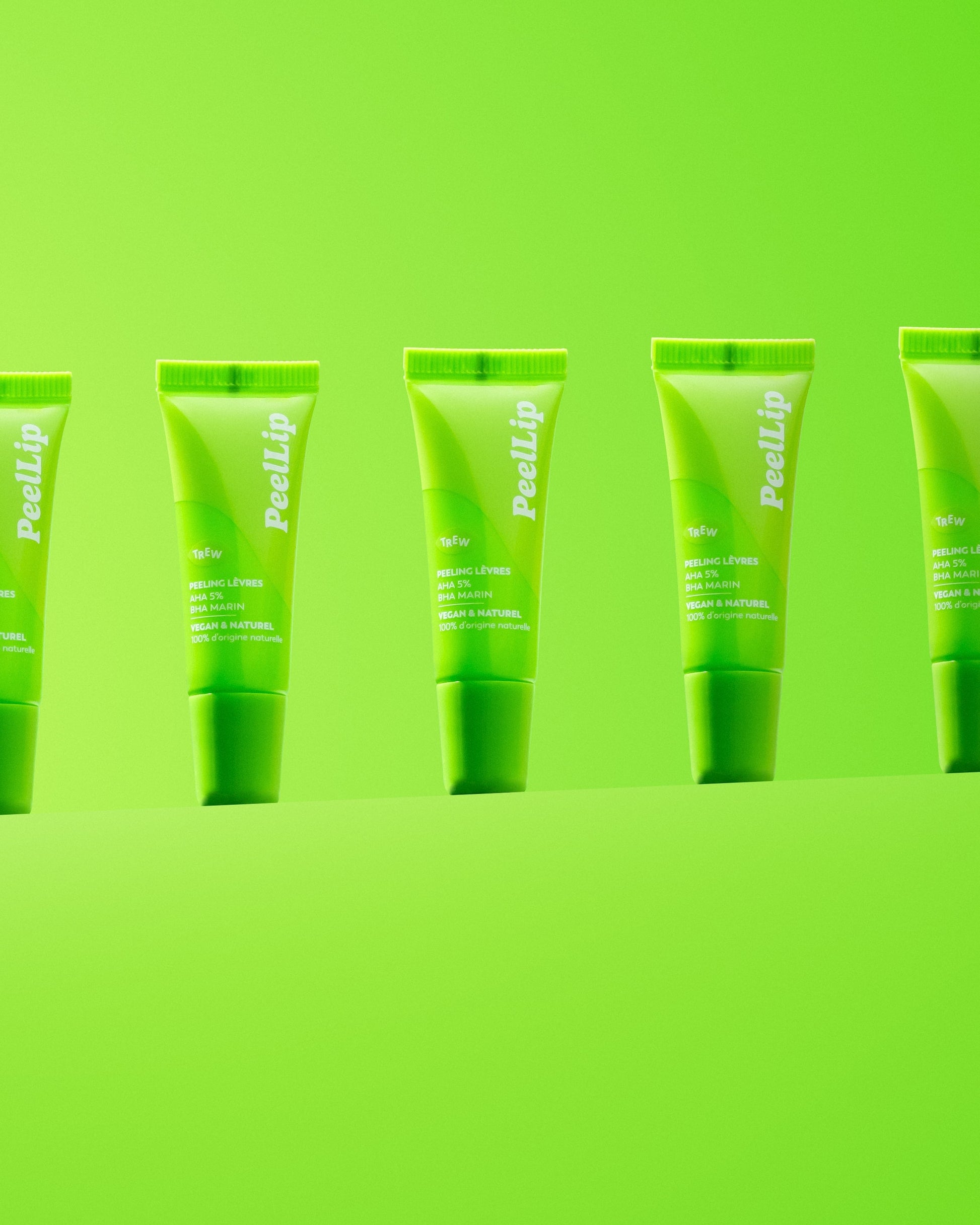 Several bright green lip exfoliant squeeze tubes standing in a row against a matching lime green background.