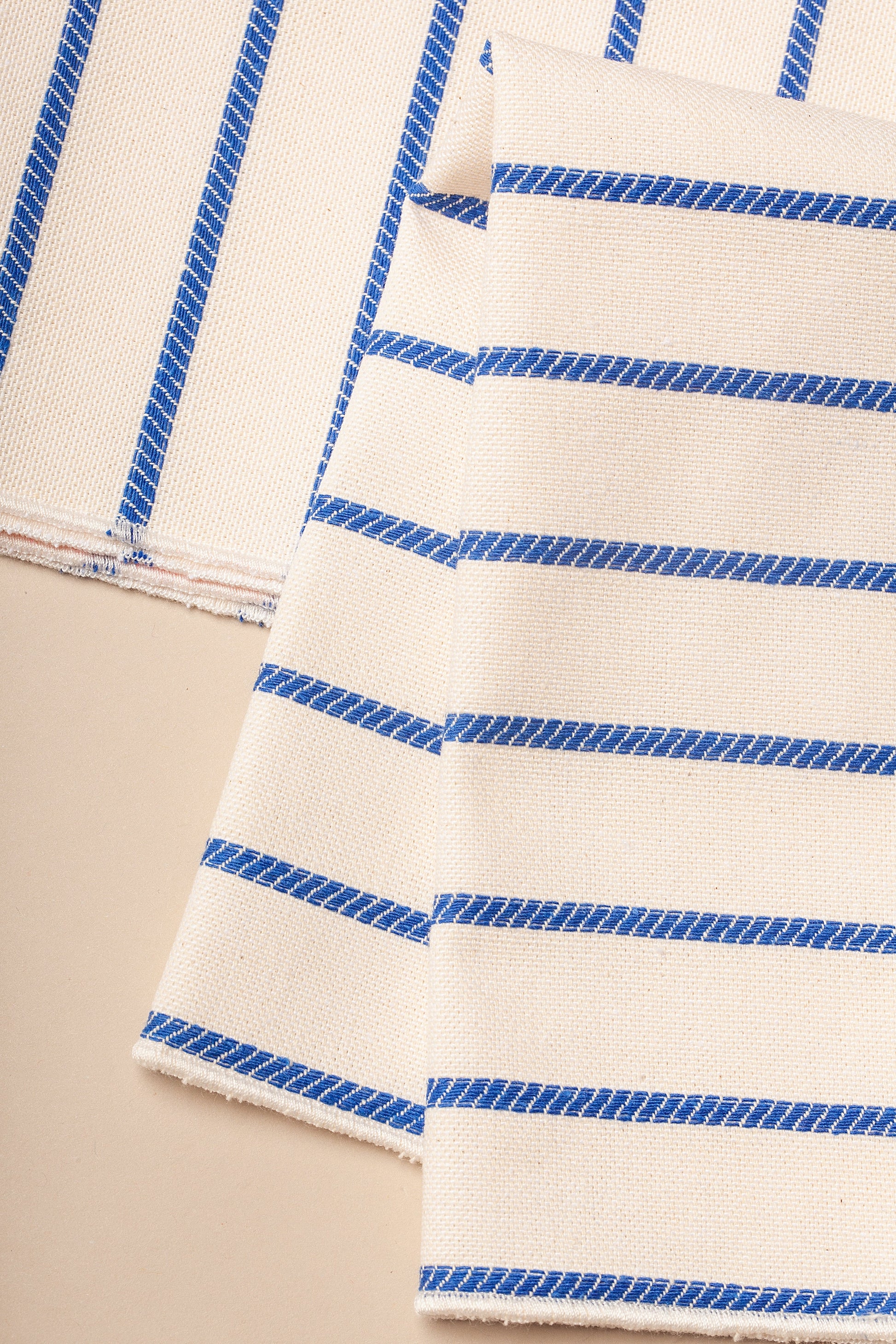 Tela de algodón beige con rayas azules, perfecta para decoración y manualidades.