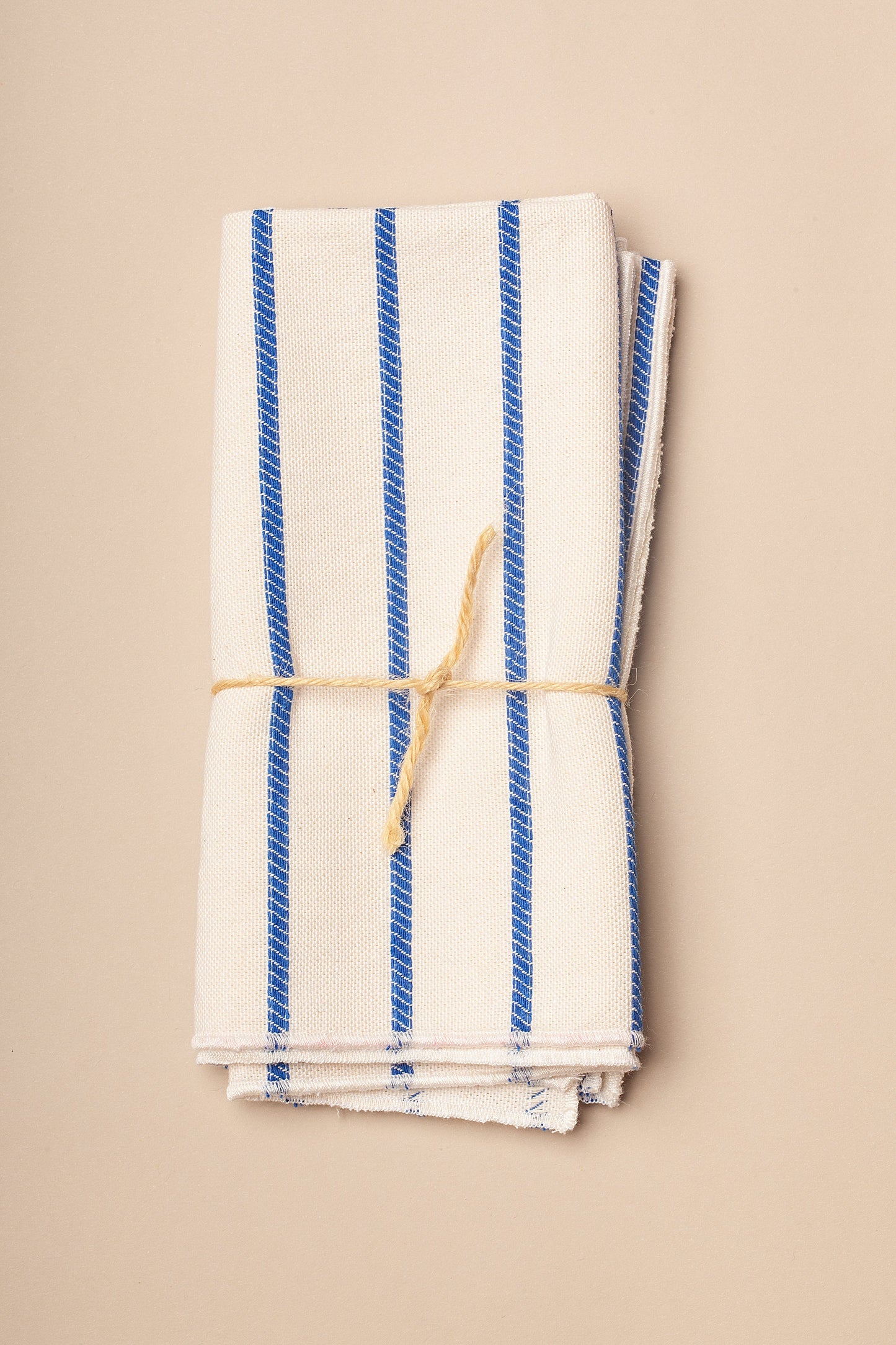 Toalla de cocina de algodón blanca con rayas azules, enrollada y atada con cuerda natural.