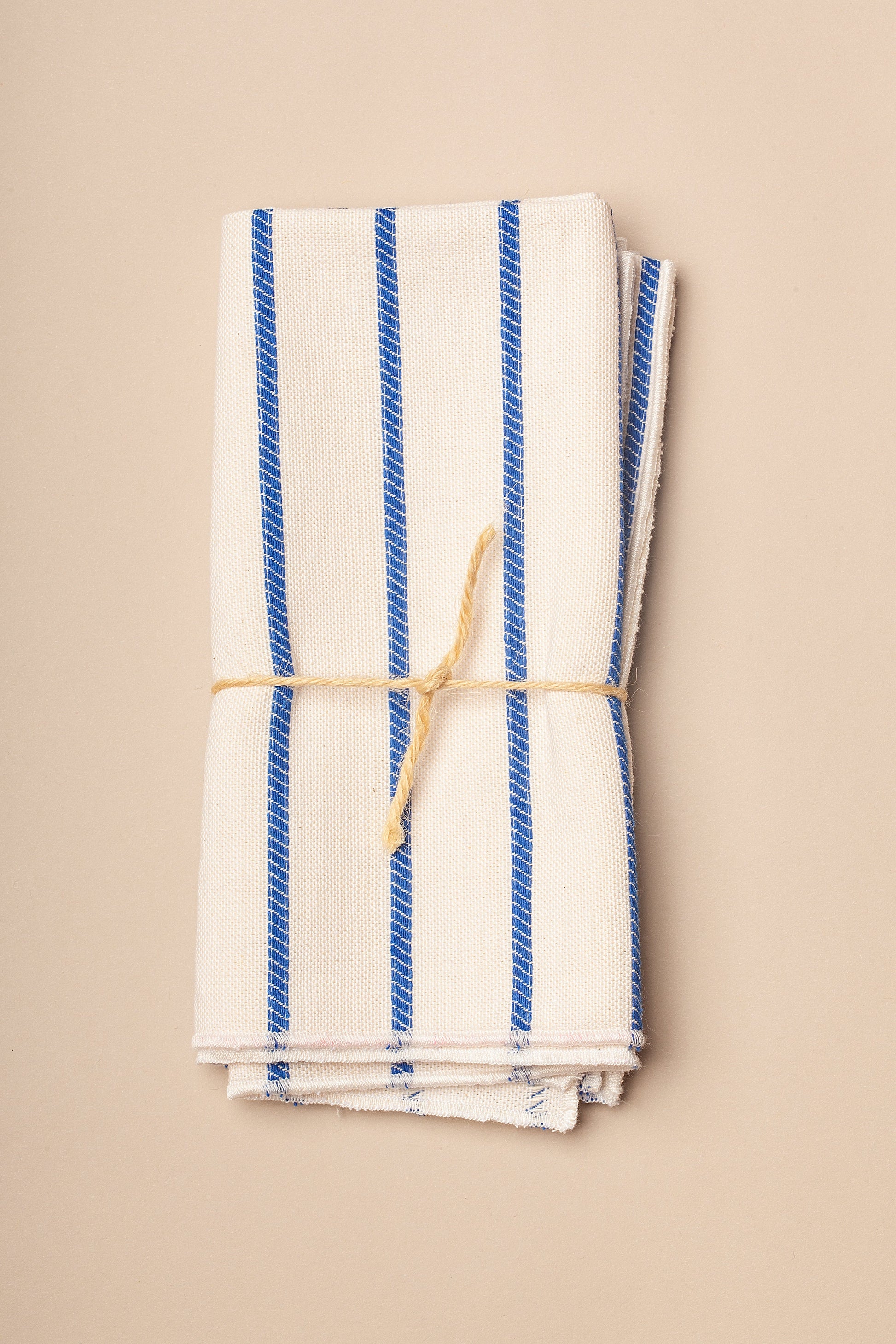 Toalla de cocina de algodón blanca con rayas azules, enrollada y atada con cuerda natural.