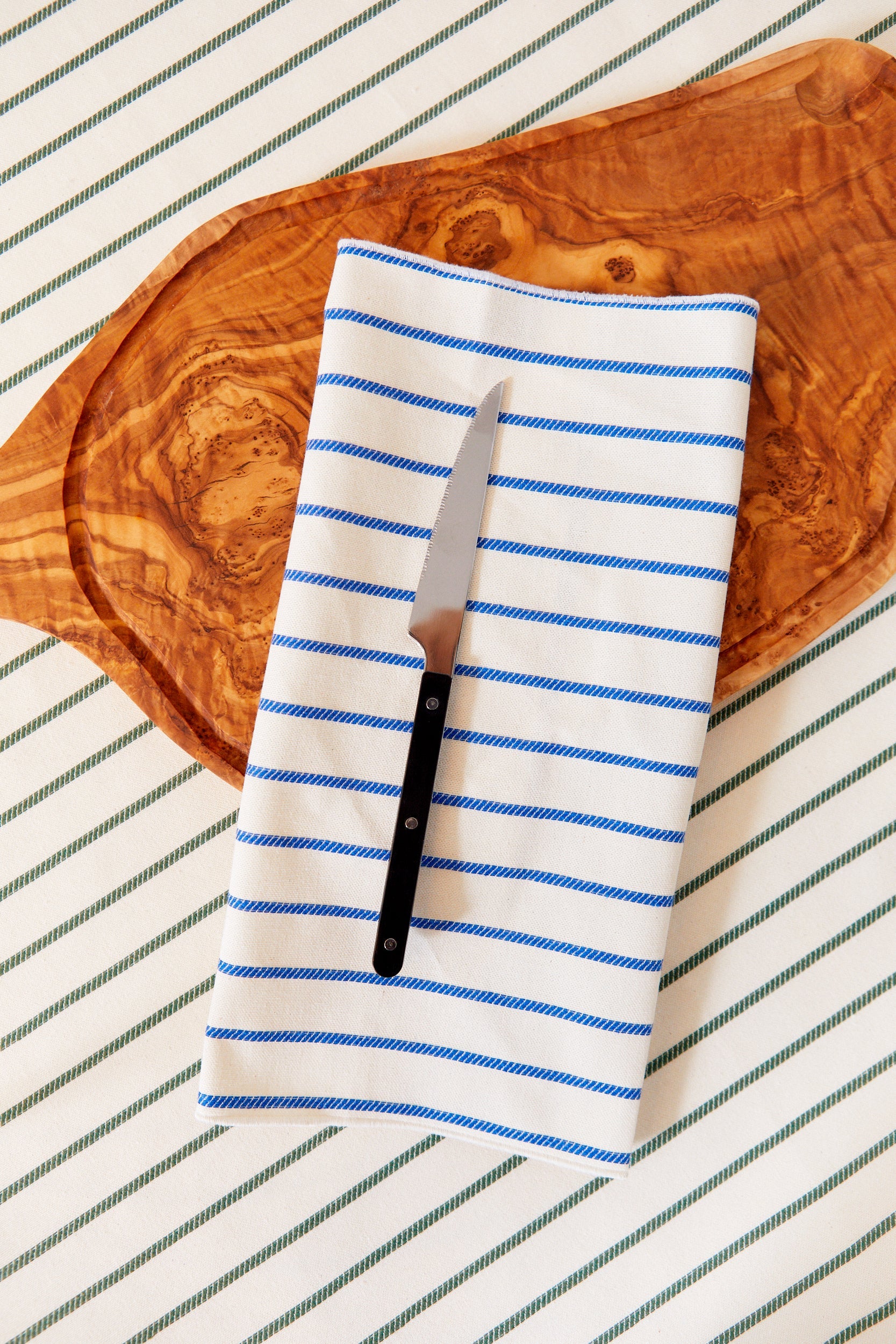 Cuchillo de cocina acero inoxidable con mango negro sobre servilleta de rayas azules y blancas, fondo de madera.
