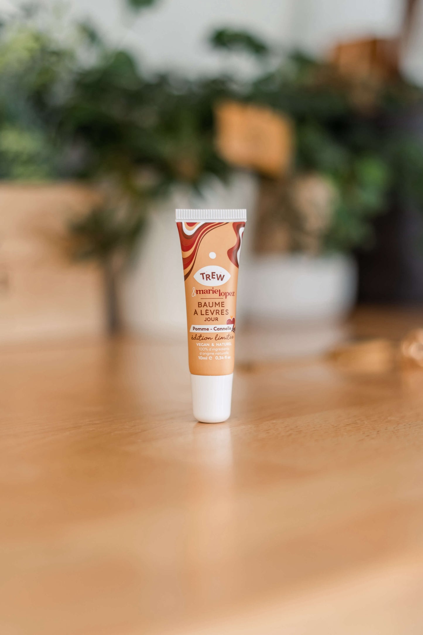 A small tan lip balm tube with a wavy brown design, standing upright on a wooden surface against a blurred backdrop.