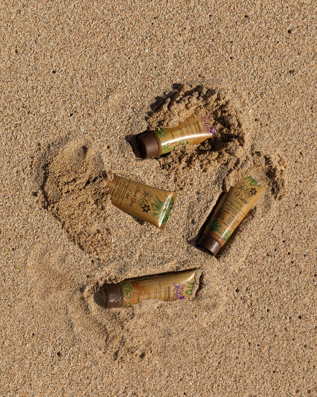 Four Bare It At The Beach tinted moisturizer tubes partially buried in sand at the beach.