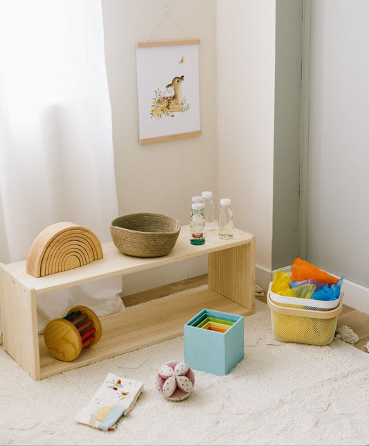 Estante de madera natural con juguetes de colores, canasta tejida y decoración infantil en una habitación luminosa.