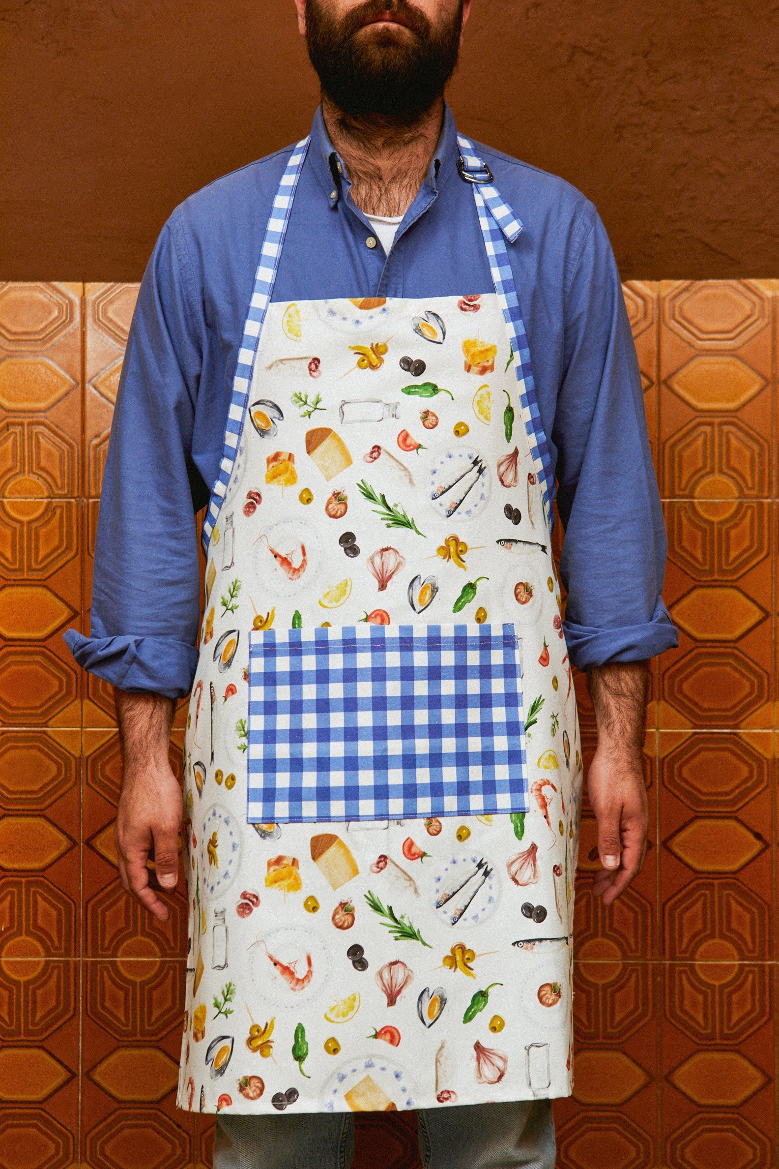 Delantal de cocina blanco con estampado de alimentos y bolsillo de cuadros azules, ideal para chefs y amantes de la cocina.