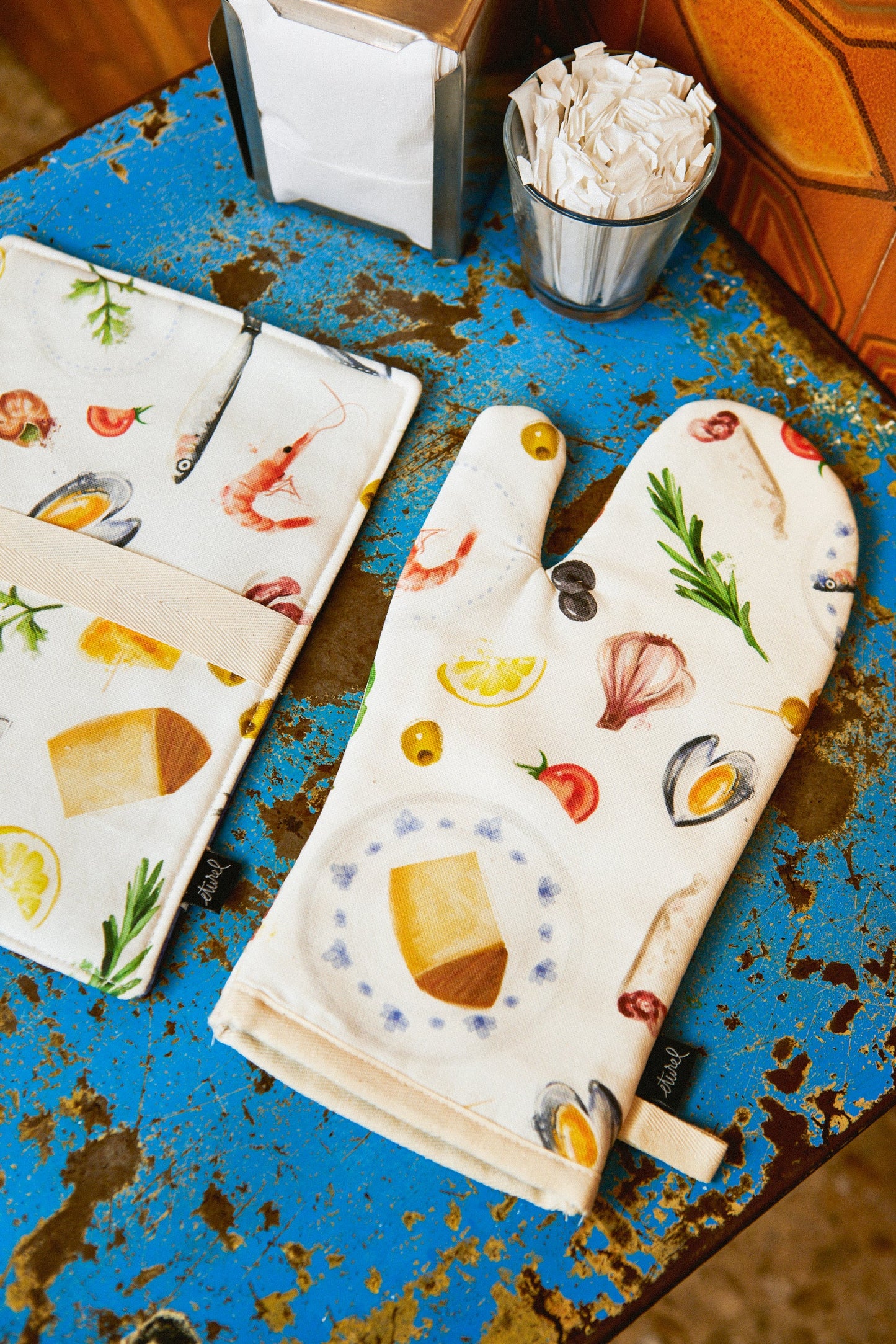 Guante de cocina blanco con estampado de alimentos, disponible en un fondo azul desgastado, estilo moderno y divertido.