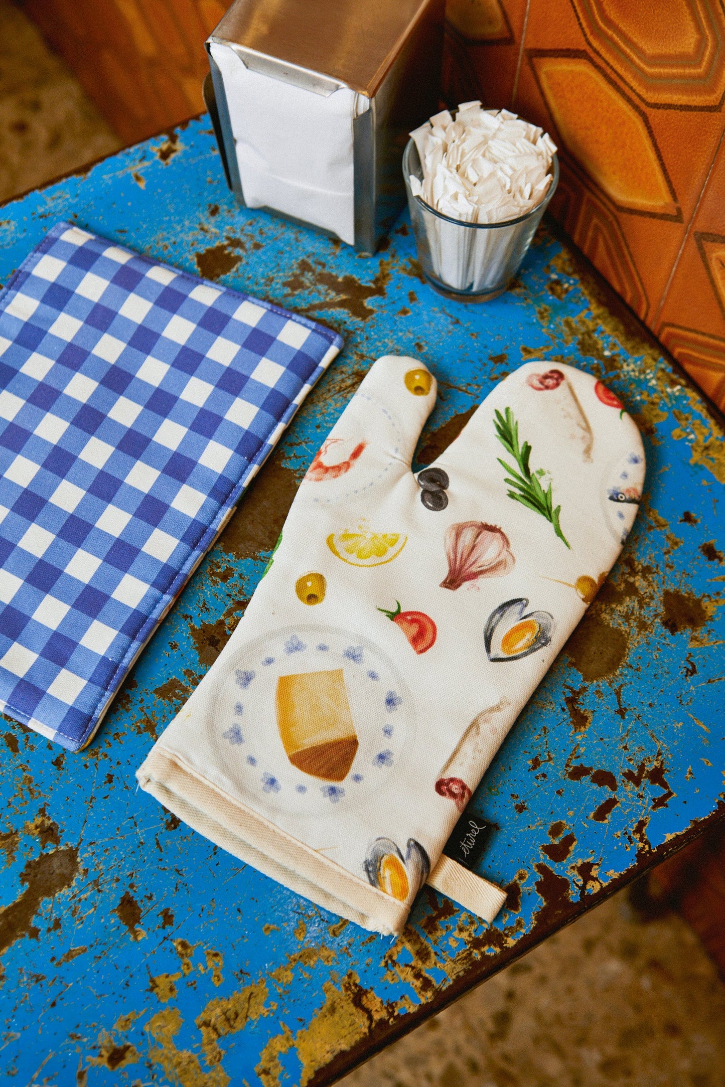 Manopla de cocina de algodón blanca con estampado de alimentos coloridos sobre fondo azul, estilo moderno y fresco.