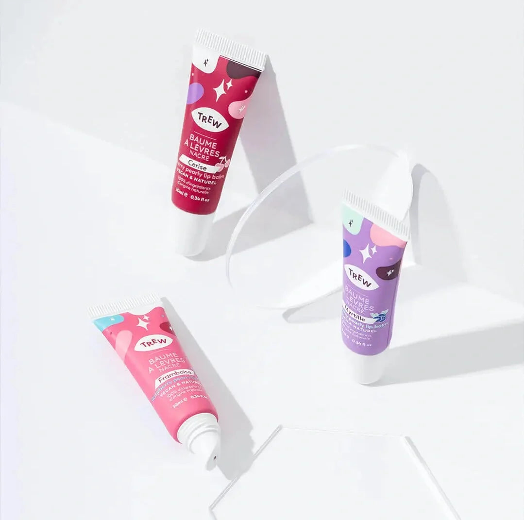 Trio de tubes de baumes à lèvres Trew colorés (rose, rouge, violet) au design ludique sur fond blanc épuré.