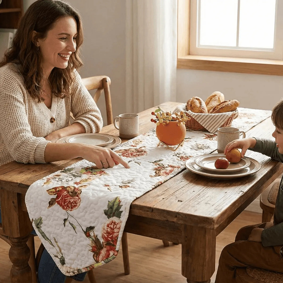 Quilted white dining table runner featuring a romantic pink and red floral rose print, laid on a wooden table.