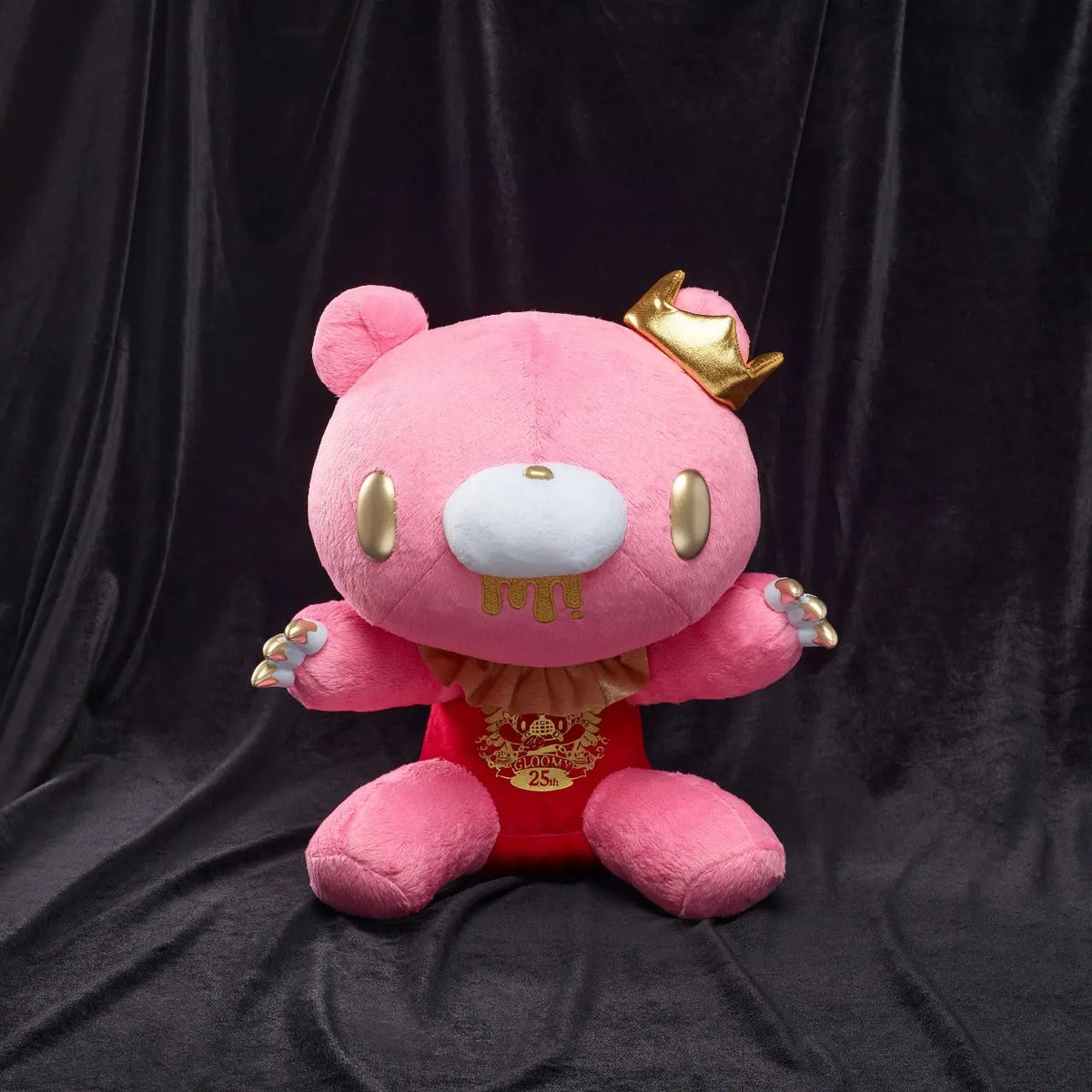 Pink Gloomy Bear plush with a gold crown, ruff, and 25th anniversary chest emblem on a black velvet background.