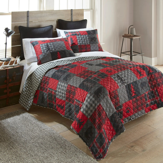 Rustic patchwork quilt set with red and grey plaid, bear, and pine tree patterns on a bed in a cabin-style room.