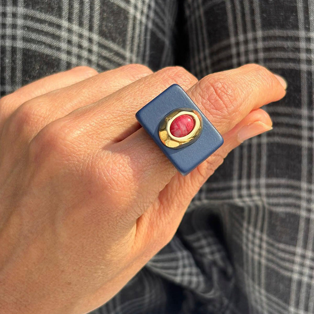 Anillo cuadrado azul con piedra rosa y detalle dorado, estilo moderno y elegante.