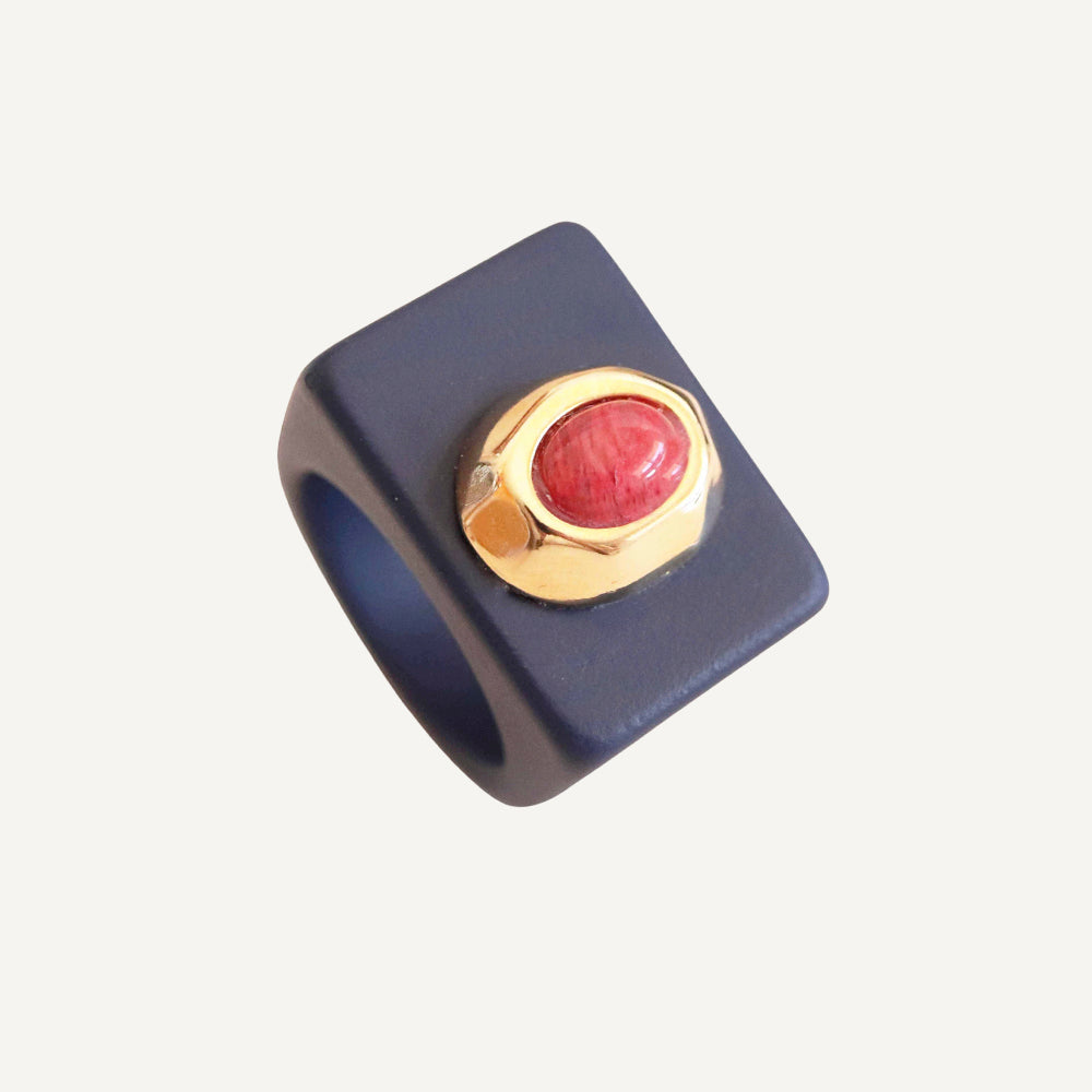 Anillo cuadrado de cerámica negra con piedra roja y adorno dorado, estilo moderno y elegante.