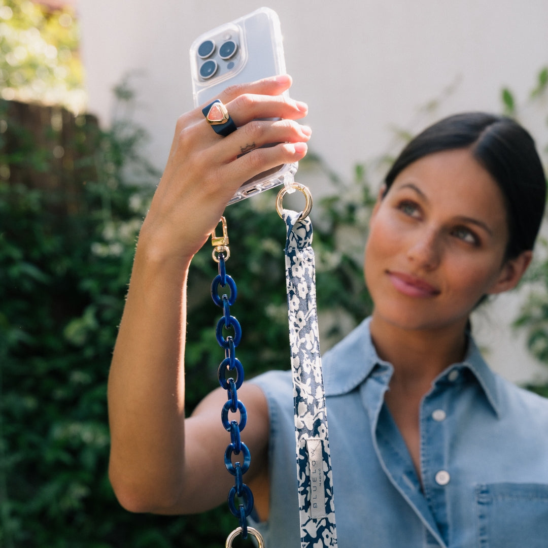 Funda de teléfono azul con cadena de eslabones y correa floral, estilo moderno y elegante.