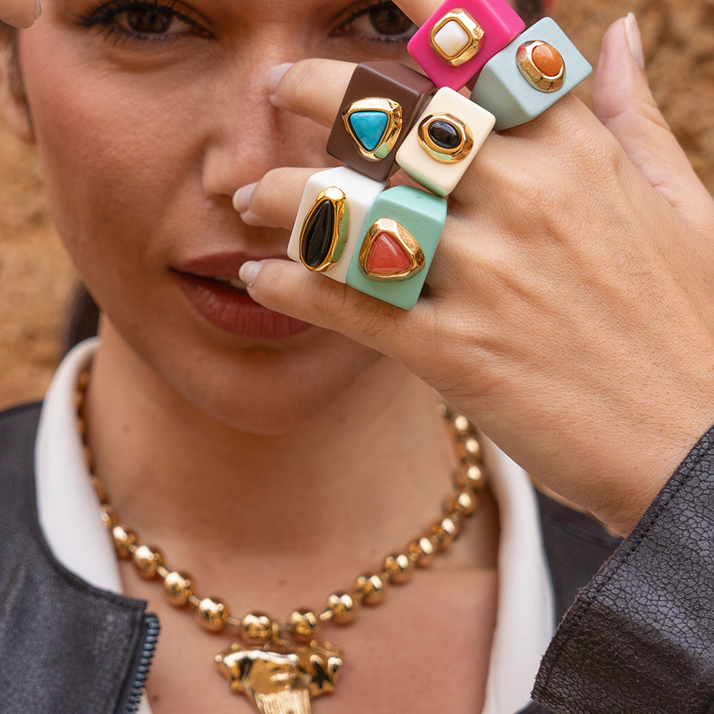 Anillos de colores pastel y tonos vibrantes con detalles en dorado, combinados con un collar de perlas doradas.