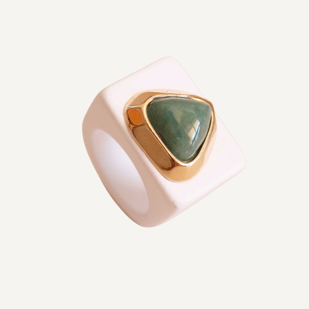 Anillo moderno de resina blanca con piedra verde en forma triangular y detalles dorados.