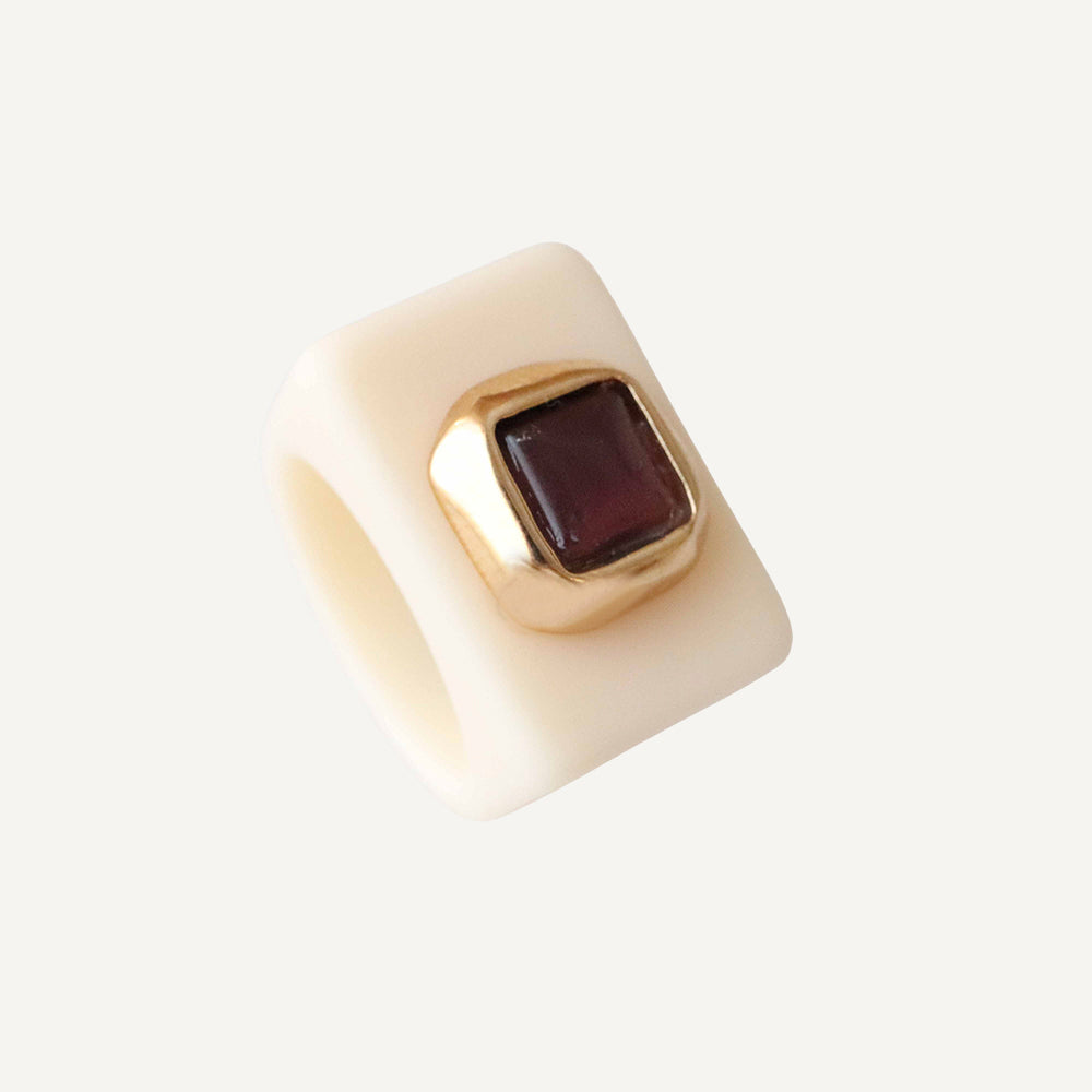Anillo de cerámica beige con piedra cuadrada burdeos y detalles en dorado. Estilo moderno y elegante.