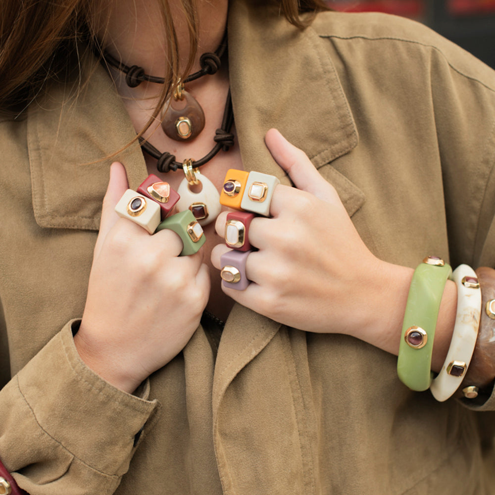 Anillos de colores pastel y pulseras de resina, estilo moderno y bohemio, con detalles dorados.