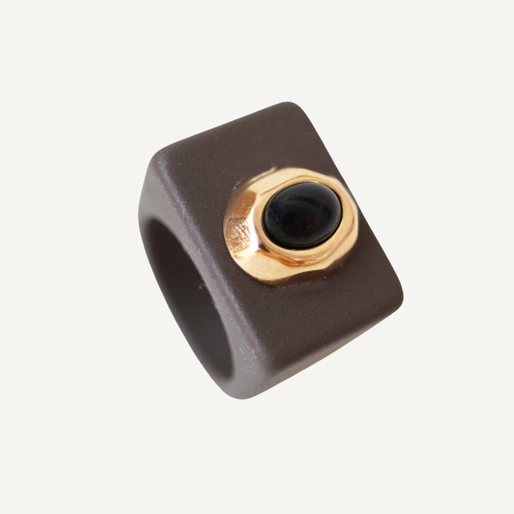 Anillo cuadrado gris con detalle dorado y piedra negra, elegante y moderno, ideal para ocasiones especiales.