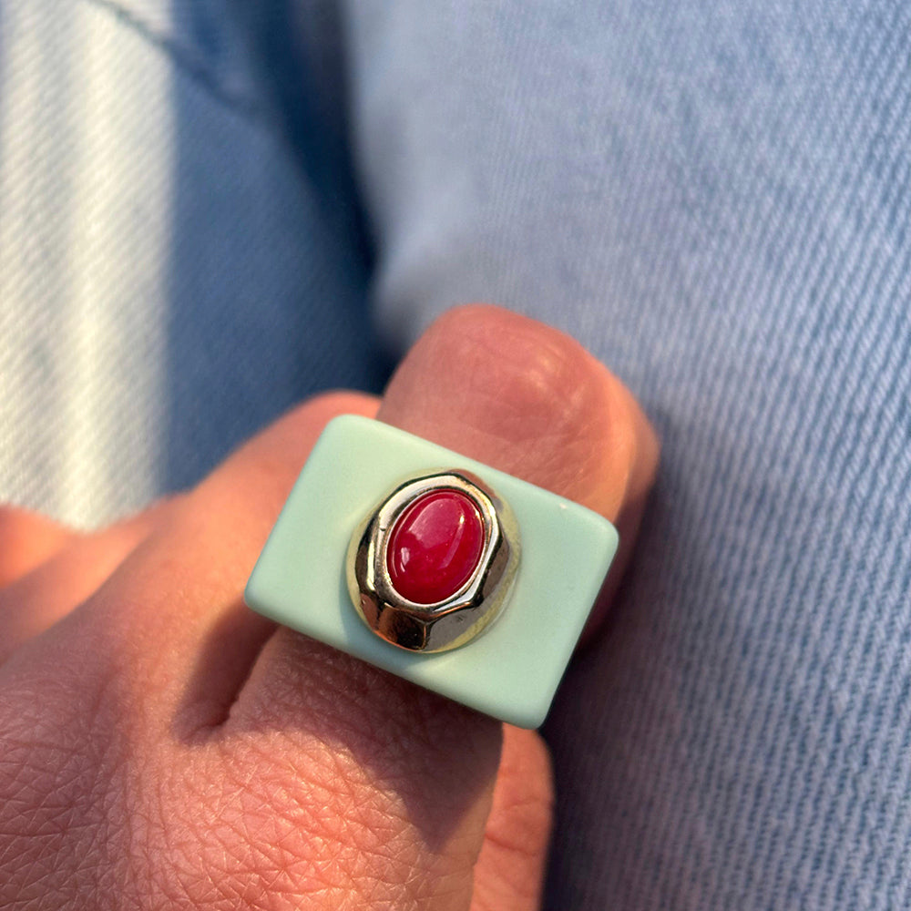 Anillo de resina celeste con piedra roja y detalle dorado, estilo moderno y elegante.
