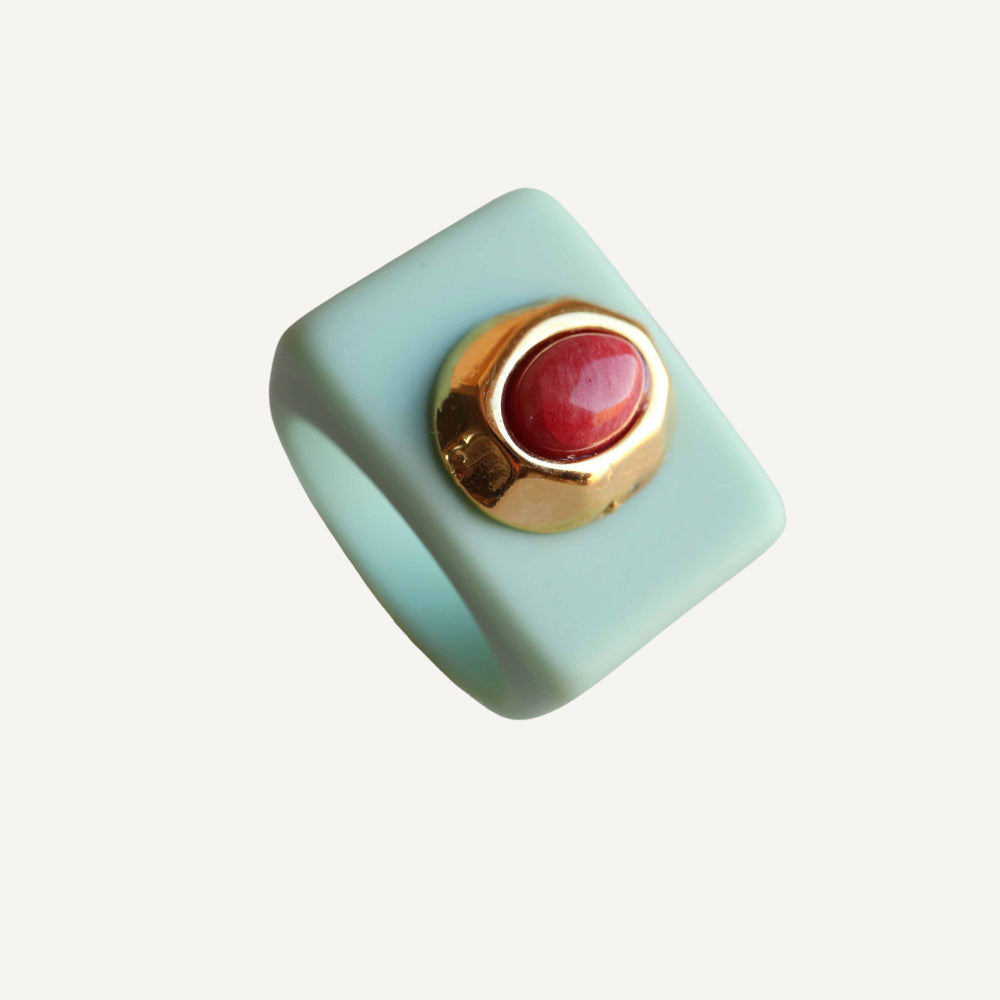 Anillo cuadrado de resina verde aguamarina con piedra roja y detalle dorado. Elegante y moderno.