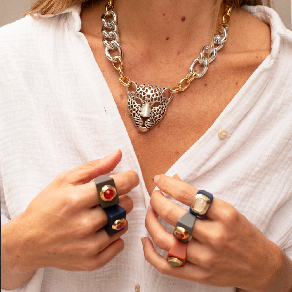 Collar de leopardo dorado y plateado con cadenas, anillos de colores azul, gris y naranja, estilo moderno y audaz.