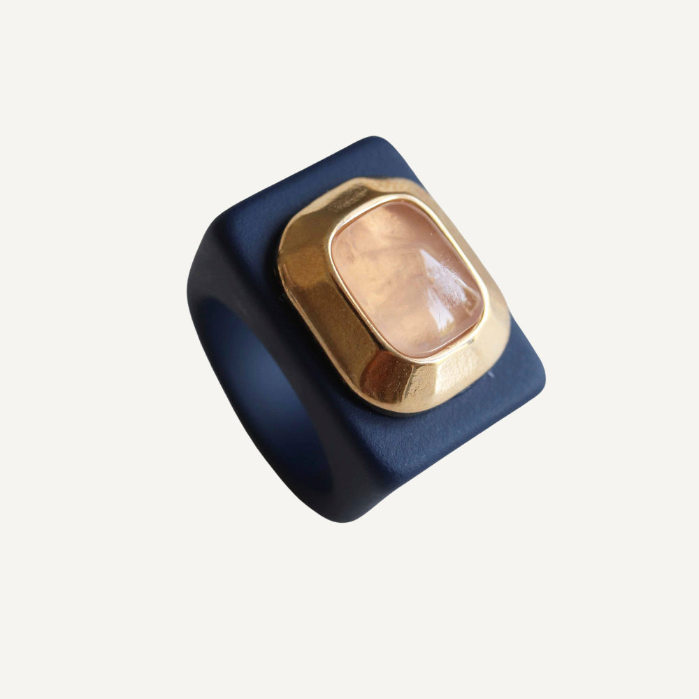 Anillo cuadrado azul con detalle dorado y piedra rosa, estilo moderno y elegante.
