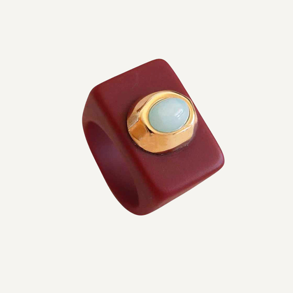 Anillo cuadrado de resina roja con detalle de piedra verde claro y acabado dorado. Ideal para un estilo contemporáneo.
