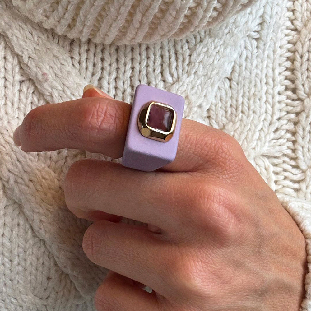 Anillo de acero dorado con gemas, diseño cuadrado en tono lavanda, ideal para un look moderno y elegante.